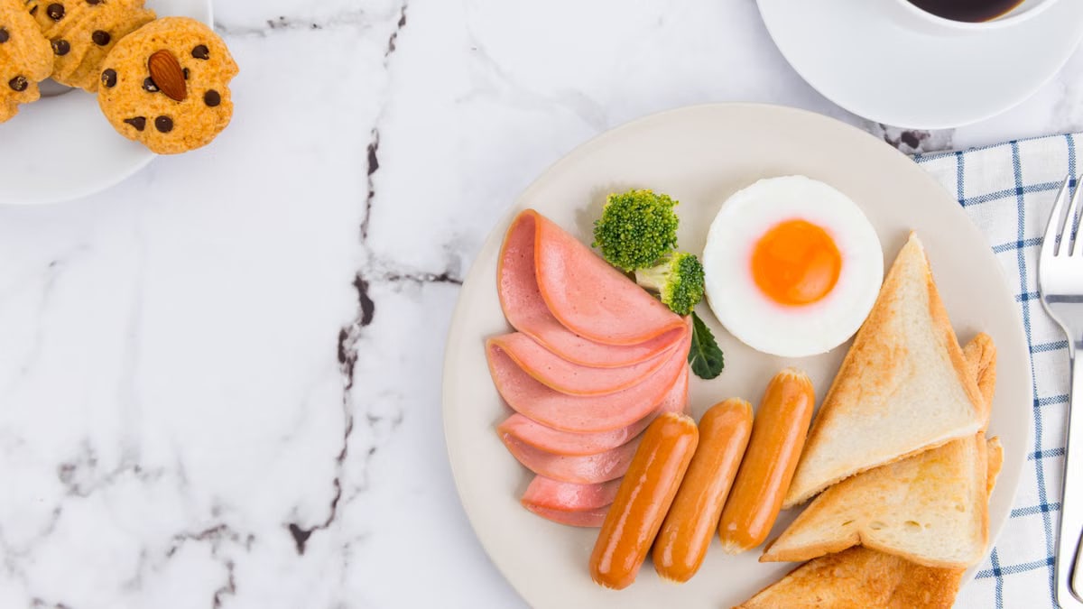 Delicious breakfast of sausages, ham, toast, egg, and coffee on a marble table.